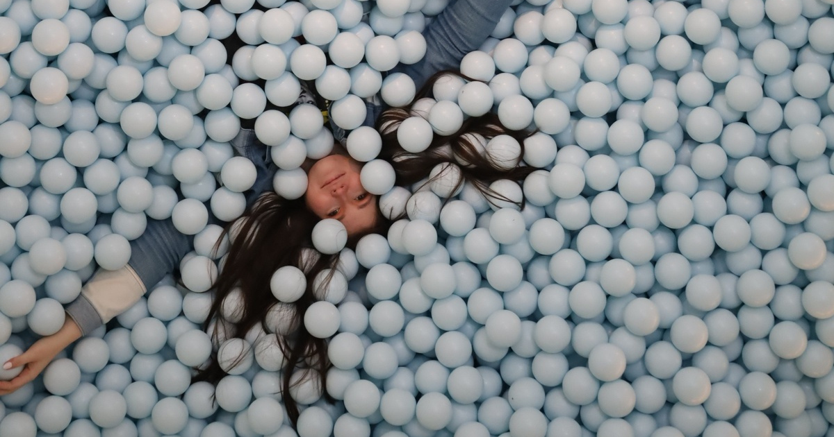 A visitor lying in the pale blue ball pit at Color Factory.