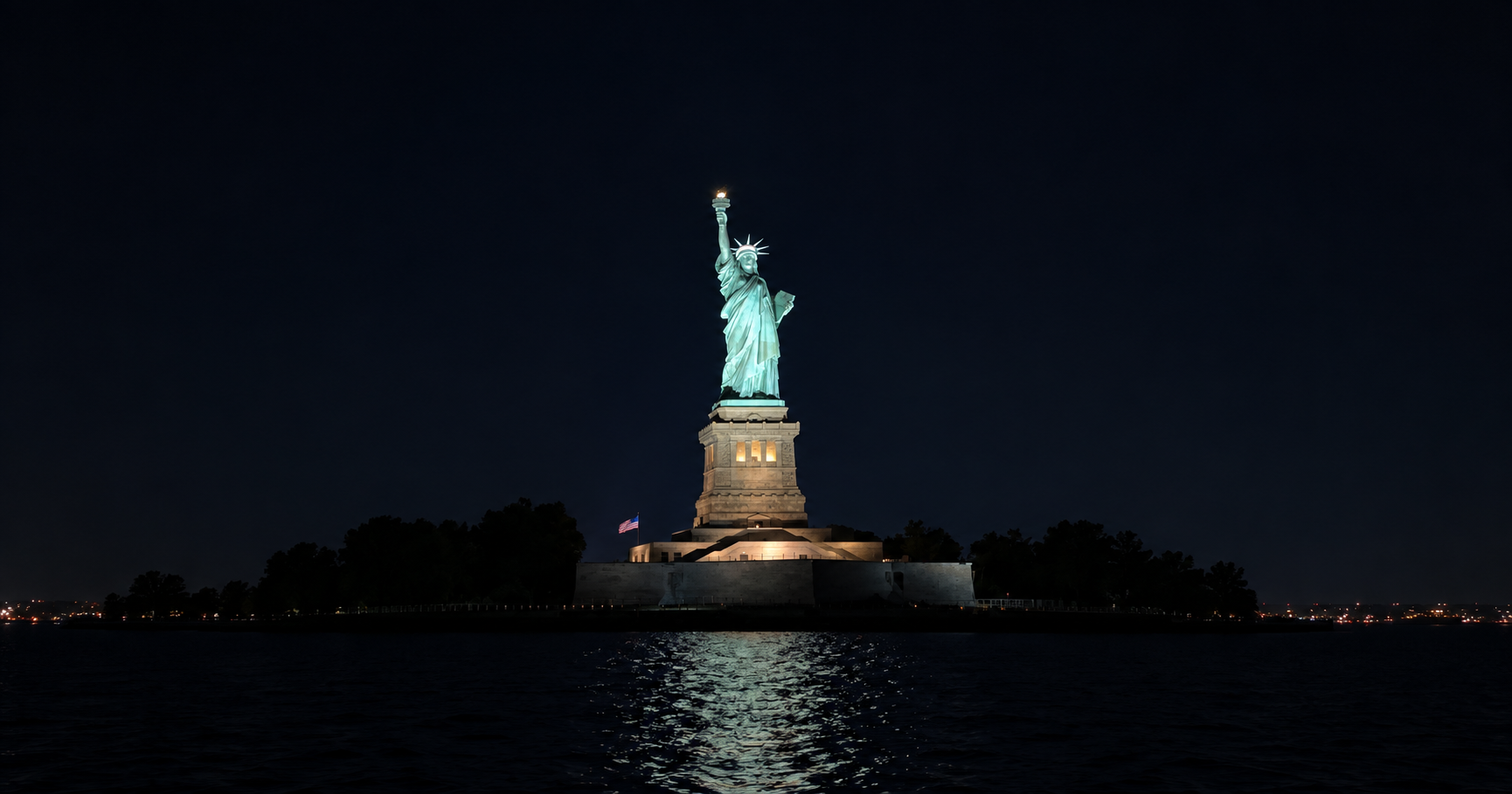 The Statue of Liberty lit up at night, seen from a harbor cruise.
