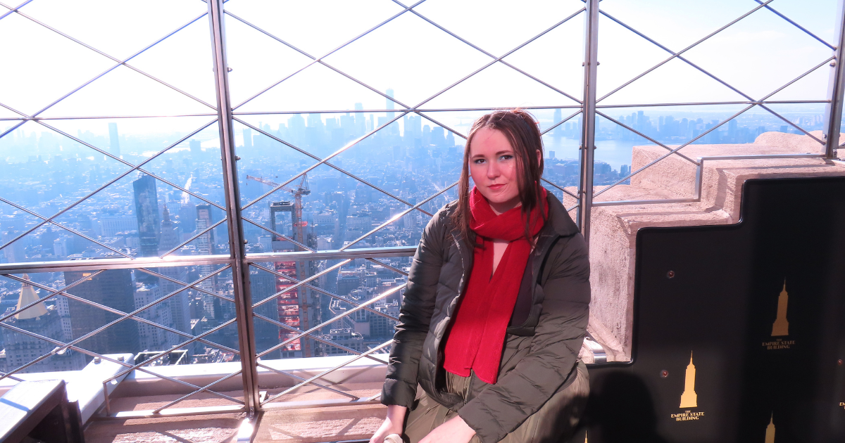 Madison Austin seated on the Empire State Building observation deck with the Manhattan skyline behind her.