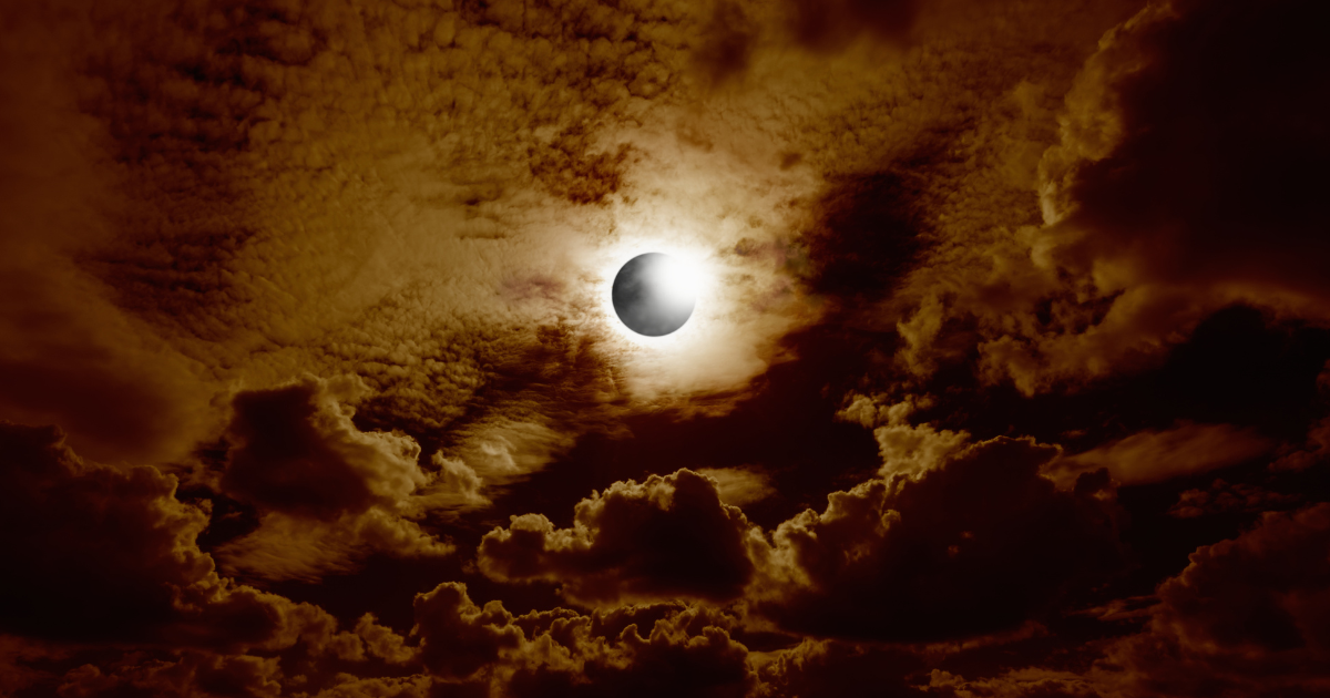 A solar eclipse surrounded by glowing light and dramatic amber clouds.